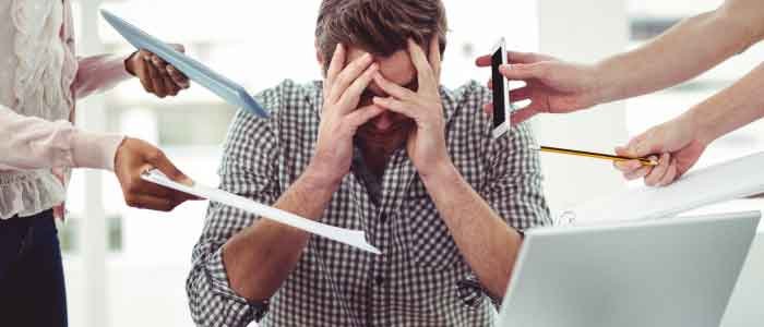 a man stressing out with his head resting on both the palms of his hands while others are giving him more work